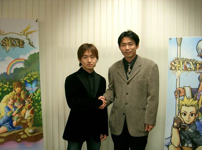 Shiomi Sawa shakes hands with an OnsOn Soft employee in front of Shine Online promotional displays.